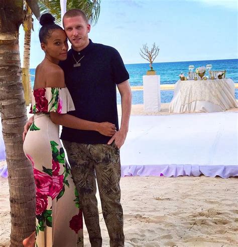 A Man And Woman Standing Next To Each Other On A Beach With The Ocean In The Background