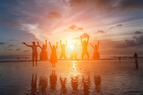 Group Of Happy Friends Jumping On Beach Against Sunset Stock Photo