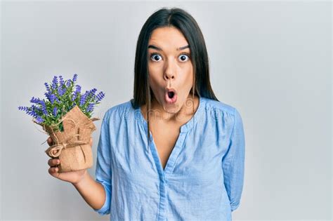 Young Hispanic Girl Holding Lavender Plant Scared And Amazed With Open Mouth For Surprise