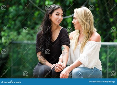 a pair of proud lesbian sitting in outdoors looking at each other and go kissing in a garden