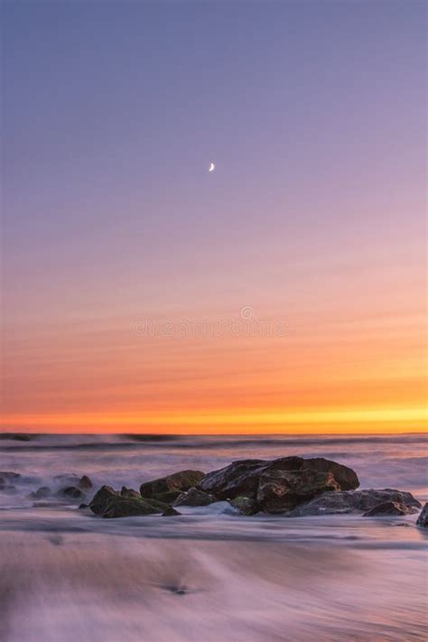 A Crescent Moon And Soft Pastel Sunset Over Waves Crashing On A Beach