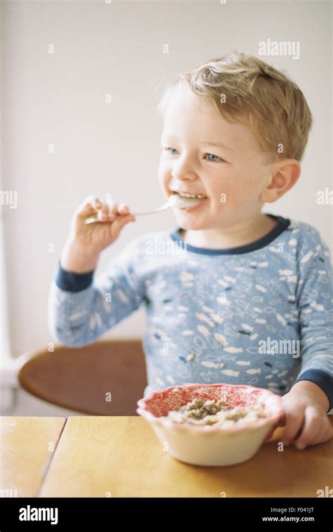 Young Boy Sitting At A Table Eating Breakfast From A Bowl Stock Photo