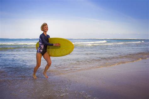 Young Attractive And Happy Blonde Surfer Girl In Beautiful Beach Carrying Yellow Surf Board