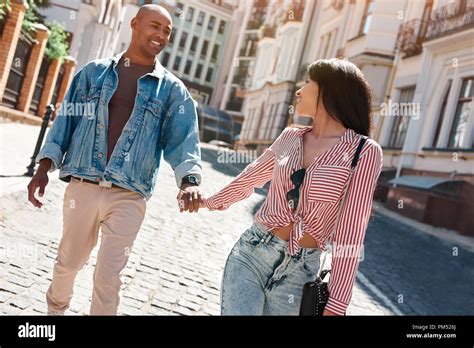 Young Diverse Couple Walking On The City Street Holding Hands Looking
