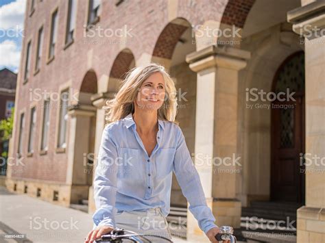 Smiling Mature Woman Riding Her Bicycle Through Vintage Town Stock