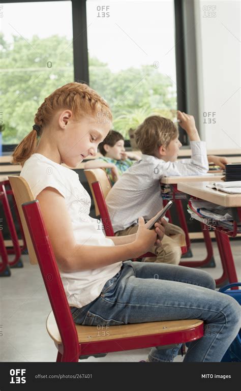 Little Girl Sitting At A Desk In A Classroom Looking At Her Phone Stock