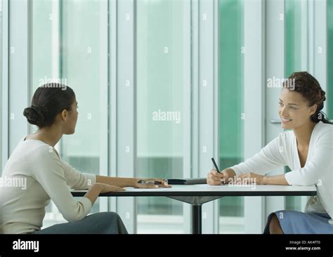 Two Women Sitting Across From Each Other At Table Working Stock Photo