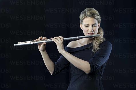 Mature Woman Playing Flute Against Black Background Stock Photo