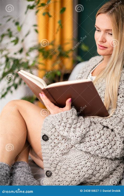 An Attractive Blonde Woman Is Sitting On The Sofa Reading A Book Stock