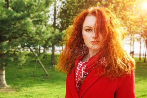 Beautiful Woman In Red Coat On The Background Of The Park Stock Photo
