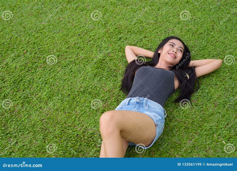 Happy Young Beautiful Asian Woman Laying Down On Grass At The Park