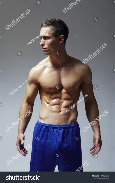 Muscular Young Man Flexing Arm Muscles In Sports Outfit On White
