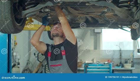 Auto Mechanic Working Underneath Car Lifting Machine At The Garage