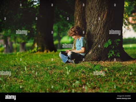 The Boy Sits Having Crossed Legs Near A Big Tree He Attentively Looks