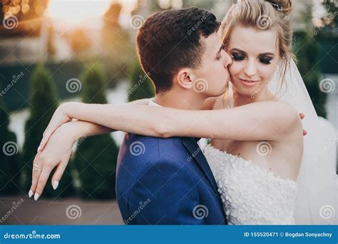 Stylish Happy Bride And Groom Kissing In Warm Sunset Light At Wedding