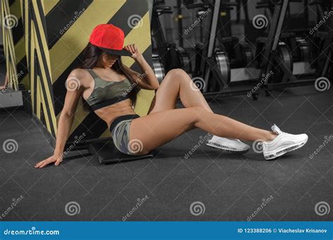 Beautiful Sporty Brunette In A Cap Sits On The Floor In The Gym After A