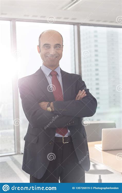 Portrait Of Smiling Businessman Standing With Arms Crossed In Boardroom