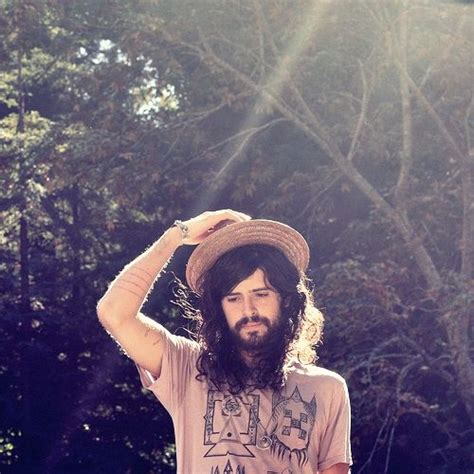 A Man With Long Hair Wearing A Hat And Standing In Front Of Some Trees