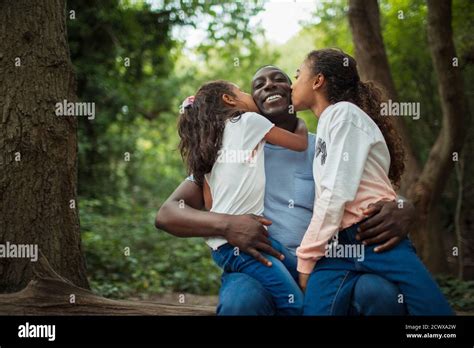 Happy Affectionate Daughters Kissing Father Below Trees In Woods Stock