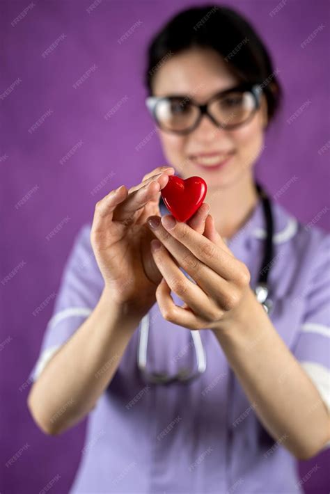 premium photo a female doctor in a blue uniform in a mask holds a small red heart as a symbol