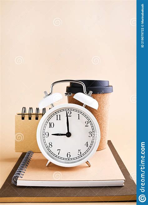 White Alarm Clock With Arrows At Nine In The Morning And Stationery