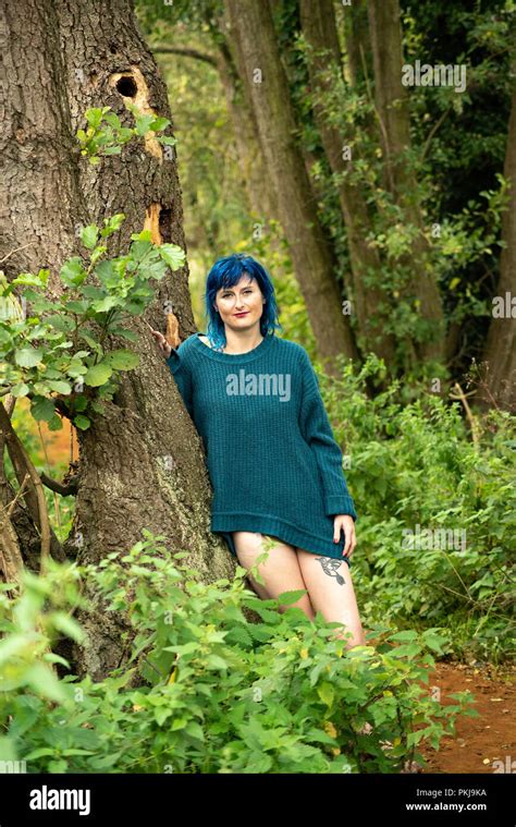 A Blue Haired Woman Wearing A Blue Jumper Leans Against A Tree Along