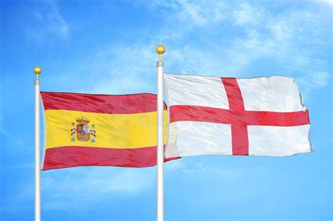 Spain And England Two Flags On Flagpoles And Blue Cloudy Sky Stock