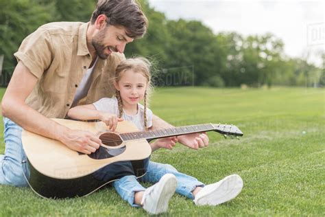 Happy Father And Daughter Playing Acoustic Guitar In Park Stock Photo
