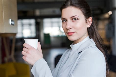 Free Photo Beautiful Businesswoman Holding Disposable Coffee Cup Looking At Camera