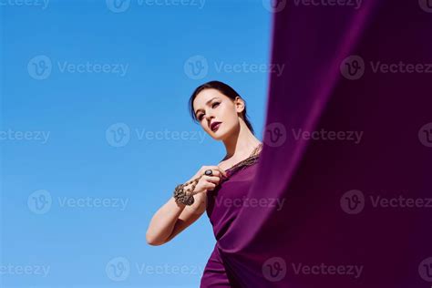 amazing beautiful brunette woman with the peacock feather in purple fabric in the desert
