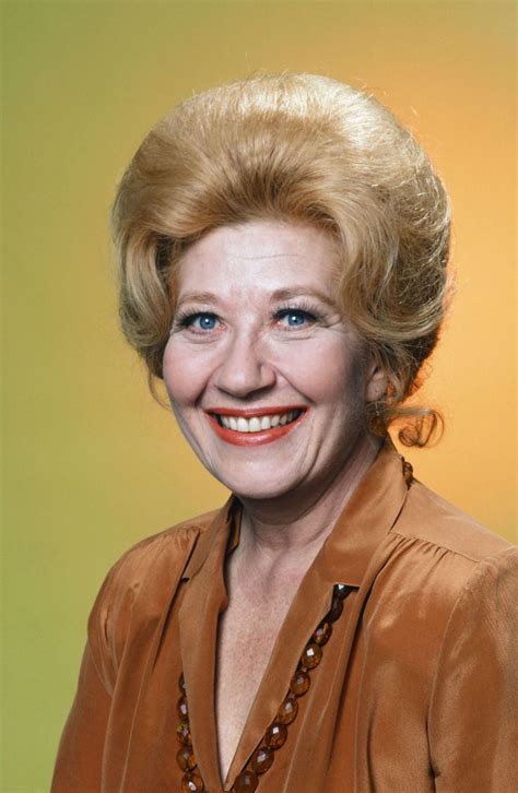 An Older Woman With Blonde Hair And Blue Eyes Wearing A Brown Blouse