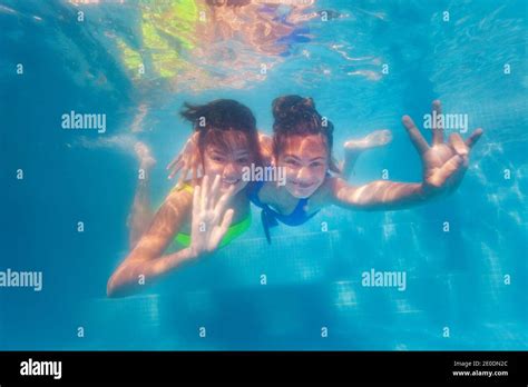 Two Happy Teenage Girls Swim Together Hugging Underwater In The Pool