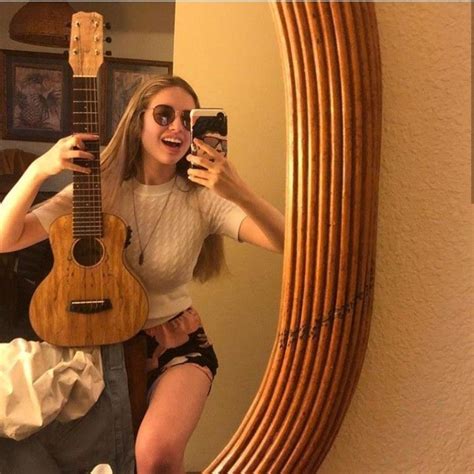 A Woman Taking A Selfie In Front Of A Mirror With Her Guitar And Cell Phone