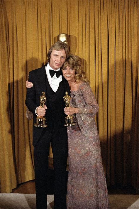 Two People Standing Next To Each Other Holding Oscars