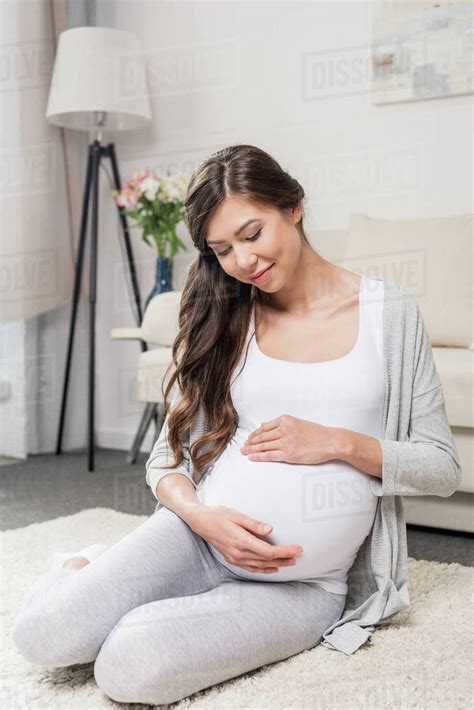 Pregnant Woman Sitting On The Floor In A Living Room Touching Her Belly
