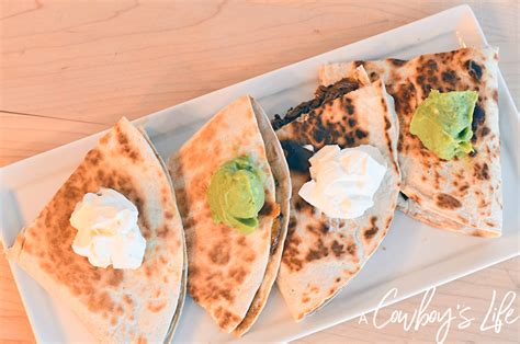 Three Quesadillas On A White Plate With Sour Cream And Avocado