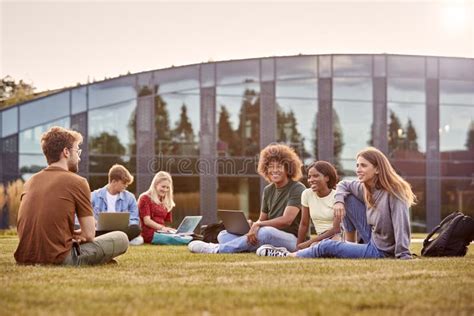 Group Of University Or College Students Sit On Grass Outdoors On Campus