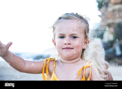 Naughty Blond Little Girl Throwing Sand In The Beach With Blue Eyes