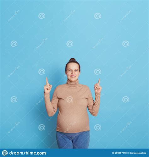 attractive european pregnant woman pointing finger up with both index fingers looks at camera
