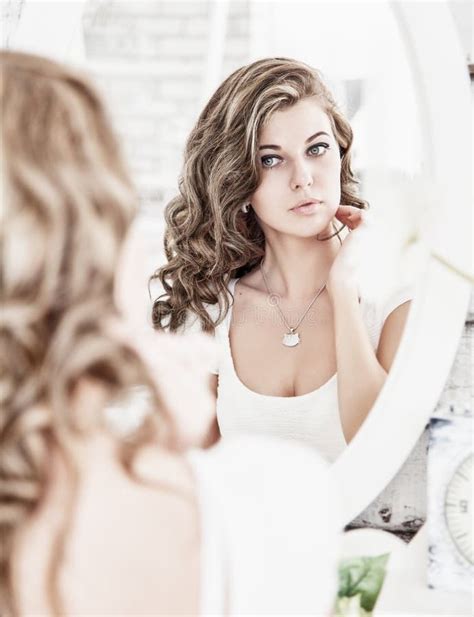 Young Beautiful Woman Looking At Her Face In The Mirror Stock Photo
