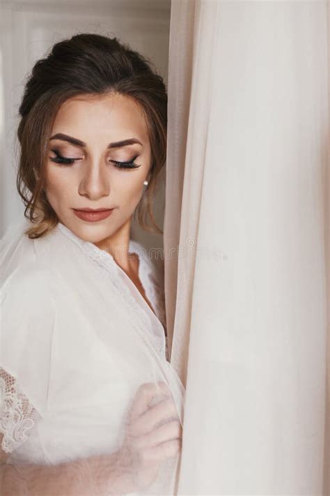 Gorgeous Bride In Silk Robe Holding Stylish Wedding Dress In Room In