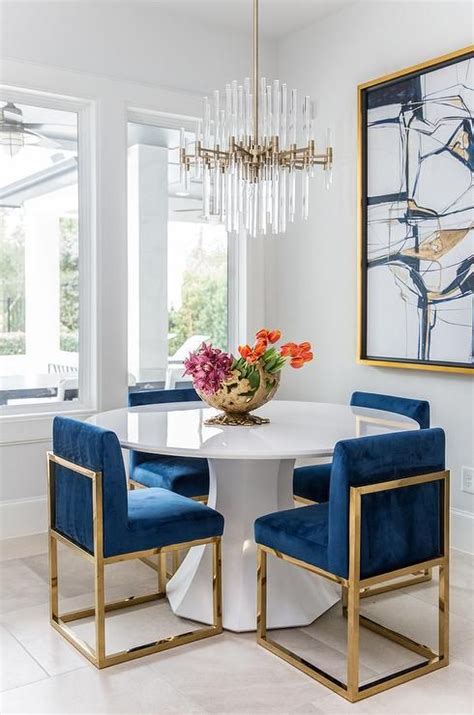 Rated 5 out of 5 stars. A round white dining table finished with gold and blue sapphire dining chairs under a brass ...