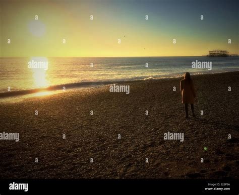 Silhouette Of Woman Standing On Beach At Sunset Hi Res Stock