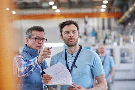 Serious Male Supervisors With Clipboard Talking In Factory Stock