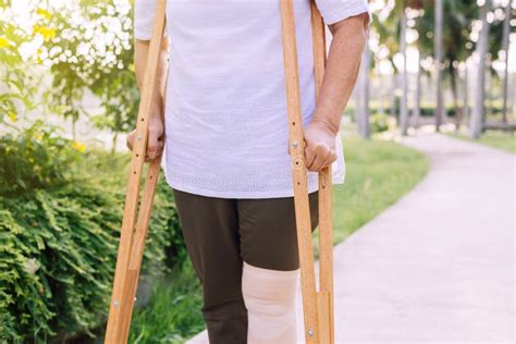 Patient Elderly Woman Using Crutches Support Broken Legs For Walking At