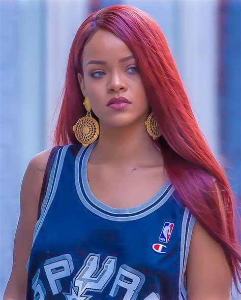 A Woman With Long Red Hair Wearing A Blue Jersey And Gold Hoop Earrings