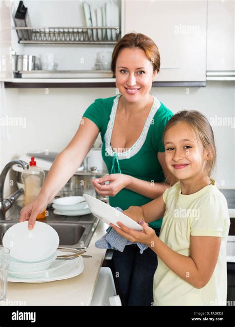 Smiling Girl Helping Mother Washing Dishes In The Kitchen Focus On