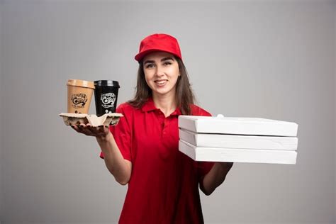 Mulher entregadora segurando pizza e xícaras de café na parede cinza