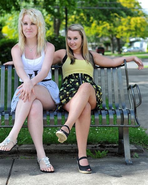 Två Unga Flickor Som Sitter På Bänk I En Parkera Som Tycker Om Sommar