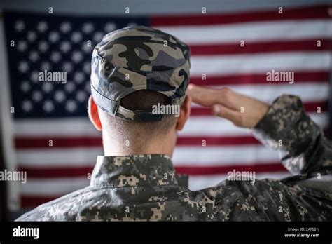 Portrait Of Serious Solider Standing In Front Of Us Flag Saluting Stock